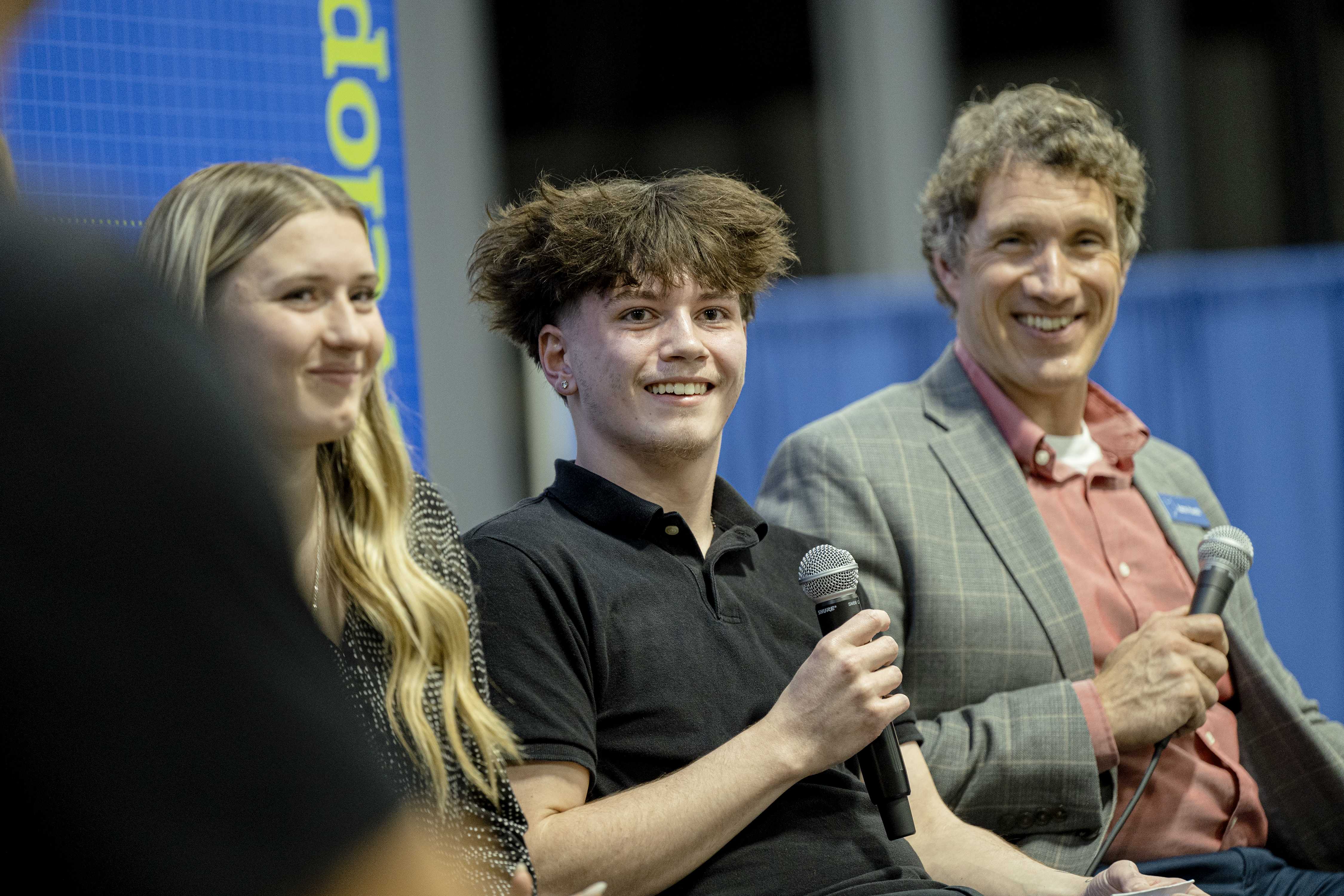 Female student and male student speaker smile on stage with employer during panel discussion